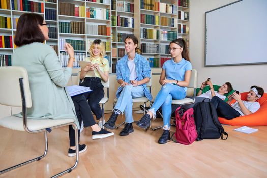 Female mentor teacher working with male teenage high school students in the library. Education, knowledge, adolescence, consultation, support, school, college concept