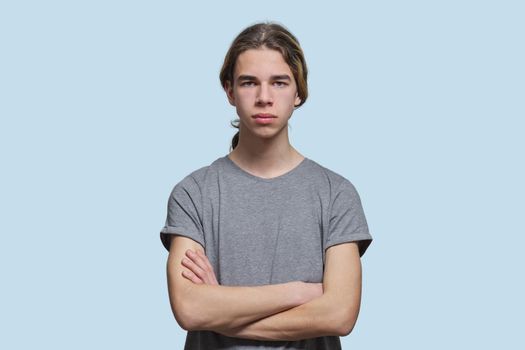 Portrait of serious guy 15, 16 years old teenager with crossed arms, handsome trendy male looking at the camera on light studio background