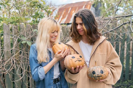 Couple of laughing teenagers with pumpkins having fun outdoors in the garden, halloween autumn holiday, youth concept