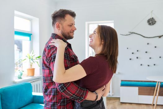 Happy romantic middle aged couple in love dancing, husband and wife dancing at home in living room, in home casual clothes. Relationships, lifestyle, communication, home life, middle-aged people