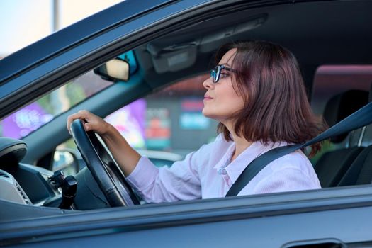 Middle-aged woman driver driving a car. Beautiful adult female with glasses, lifestyle, people, transport concept