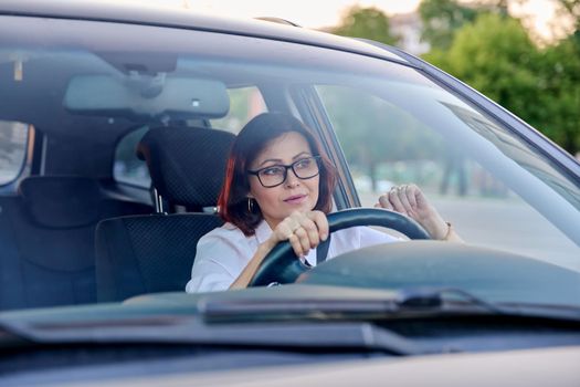 Middle-aged woman driver with glasses, female driving a car. Mature people, transportation, lifestyle concept