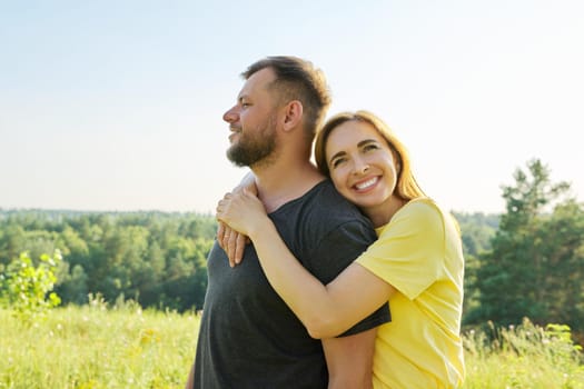 Portrait of happy middle-aged couple on summer sunny day. Beautiful people man and woman embracing in nature, family, happiness, holidays, joy concept. Copy space