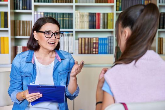 Woman school psychologist, teacher, social worker, mentor working with a teenage girl in the library, office with books. Social assistance, mental health, adolescence, therapy, psychology concept