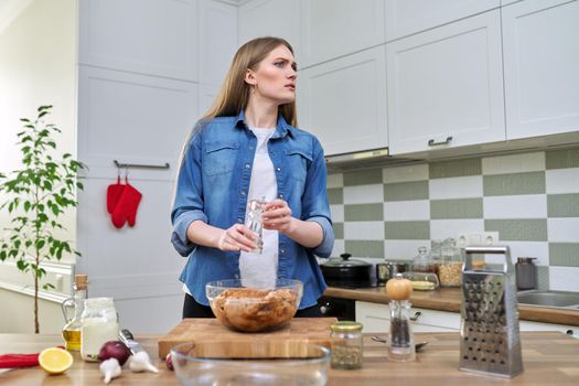 Young woman cooking chicken for holiday, marinating with spices with black pepper salt, at home in kitchen. Culinary blog, recipe, hobby and leisure.