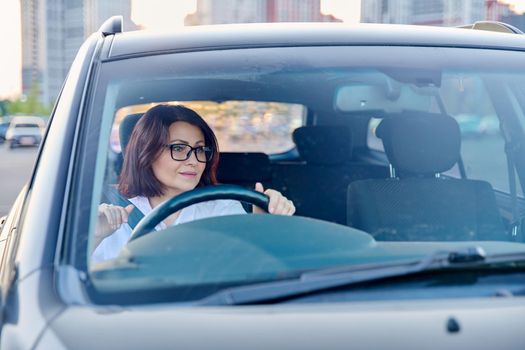 Middle-aged woman driver with glasses, female driving a car. Mature people, transportation, lifestyle concept