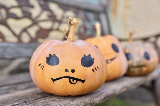 Halloween three pumpkins outdoor, nobody, pumpkins with painted eyes smile on wooden old bench in autumn garden, Halloween celebration, seasonal festive decoration