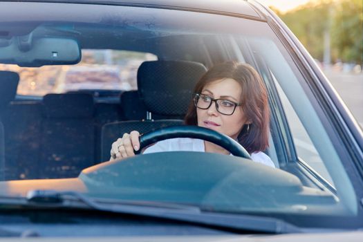 Middle-aged woman driver with glasses, female driving a car. Mature people, transportation, lifestyle concept