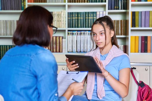 Woman school psychologist teacher mentor talking and helping student, girl teenager, in office near bookcase. Mental health of adolescents, psychology, social issues, professional help of counselor