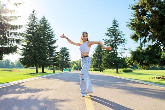 Dancing young female teenager on road in park on sunny summer day. Hipster teen girl in jeans dancing sports street dance. Youth, teens, summer, fashion, street style, lifestyle concept