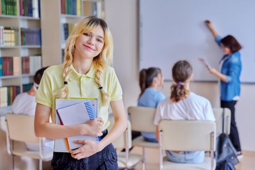 Female teenager student smiling looking at camera, group of pupils and teacher in library. High school, college, knowledge, education, adolescence concept