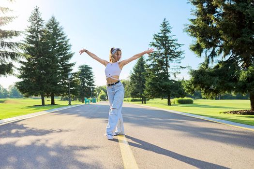 Dancing young female teenager on road in park on sunny summer day. Hipster teen girl in jeans dancing sports street dance. Youth, teens, summer, fashion, street style, lifestyle concept