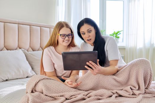 Communication relationship parent mom and child daughter teenager. Mother and daughter sitting together with digital tablet, looking at gadget screen, laughing, using video call, online meeting