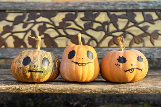 Halloween three pumpkins outdoor, nobody, pumpkins with painted eyes smile on wooden old bench in autumn garden, Halloween celebration, seasonal festive decoration