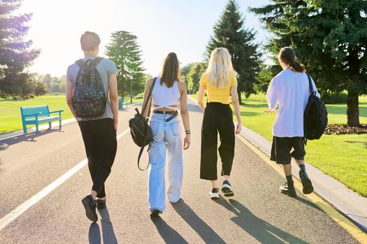 Outdoor, four teenagers walking together on road. Group of happy teenage friends on sunny summer day, back view. Adolescence, youth, friendship, young people, high school college concept