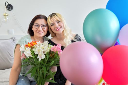 Portrait of happy smiling mom and teenage daughter, birthday celebration, women with bouquet of flowers colored balloons. Holiday, birthday, parent teenager relationship concept