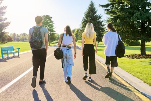 Outdoor, four teenagers walking together on road. Group of happy teenage friends on sunny summer day, back view. Adolescence, youth, friendship, young people, high school college concept