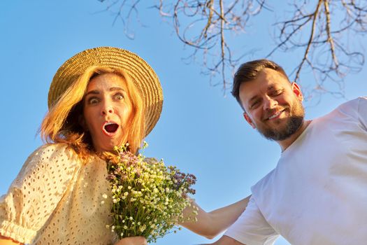 Surprised adult couple, man and woman in their 30s and 40s looking at the camera with emotion of surprise, blue sky background, looking down at the camera