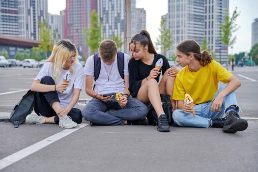 Group of teenagers with ice cream looking together at smartphone screen, urban style, modern city background. Trending youth, friendship, lifestyle, fun, adolescence concept