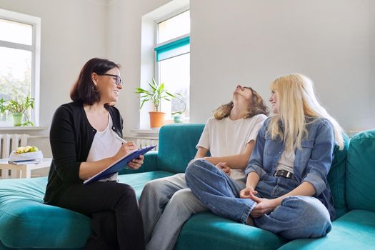 Professional female social worker, teacher, counselor, psychologist talking with teenagers, discussing school projects, organizing activities. Smiling, positive college and high school students