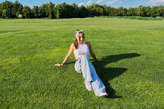 Girl hipster teenager lying on grass, green lawn and blue sky background. Summer, vacation, nature, beauty, relax, lifestyle, leisure, youth concept