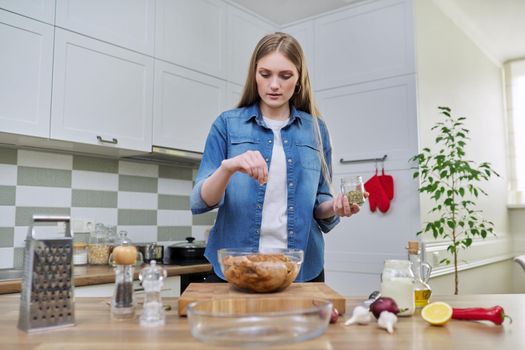 Young woman cooking chicken for holiday, marinating with spices with black pepper salt, at home in kitchen. Culinary blog, recipe, hobby and leisure.