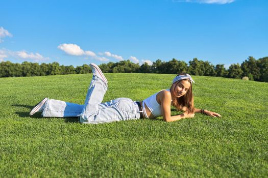 Girl hipster teenager lying on grass, green lawn and blue sky background. Summer, vacation, nature, beauty, relax, lifestyle, leisure, youth concept