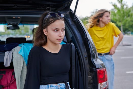 Portrait of a beautiful teenage girl of fourteen years. Adolescent female near the car, city guy friend background.