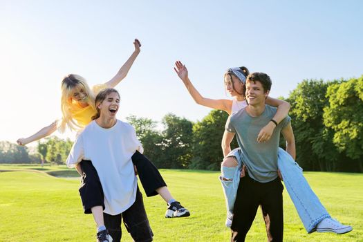 Happy group of teenagers having fun outdoors. Two young laughing couples of teenage friends, outdoors in park, green lawn grass background, sunny summer day. Adolescence, youth, friendship, young people