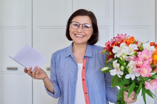 Happy middle age woman with bouquet of flowers looking into the camera with paper text congratulation. Congratulations, date, surprise, happiness, joy, celebration