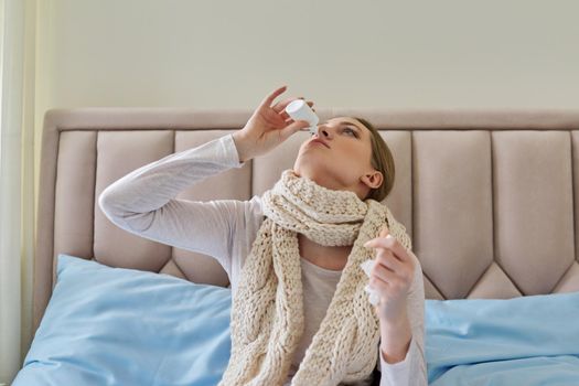 Sick woman at home in bed using nasal drops. Medicine, pharmacology, flu season, seasonal diseases, people concept