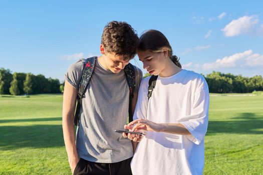 Teenagers friends talking looking at smartphone screen. Two guys 16, 17 years old with smartphone outdoors, on road on sunny summer day. Technology, lifestyle, friendship, youth, adolescence concept