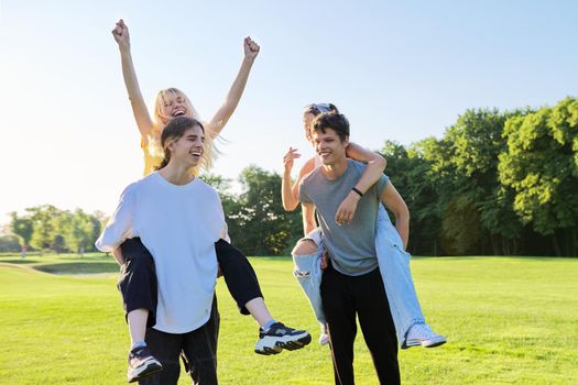 Happy group of teenagers having fun outdoors. Two young laughing couples of teenage friends, outdoors in park, green lawn grass background, sunny summer day. Adolescence, youth, friendship, young people