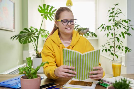 Teenage girl and pet green quaker parrot on the shoulder. Young female student doing school lessons at home in the company of a friend's bird