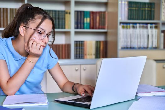 Girl teenager 14, 15 years old with glasses studies in library, using laptop. Education, knowledge, adolescence, school concept