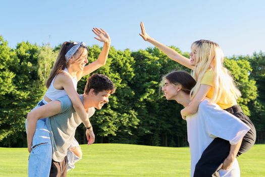 Happy group of teenagers having fun outdoors. Two young laughing couples of teenage friends, outdoors in park, green lawn grass background, sunny summer day. Adolescence, youth, friendship, young people