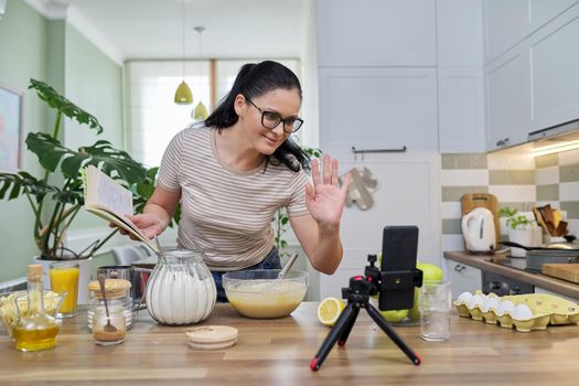Woman recording recipe for making apple pie. Female food blogger in kitchen talking looking at webcam using smartphone on tripod