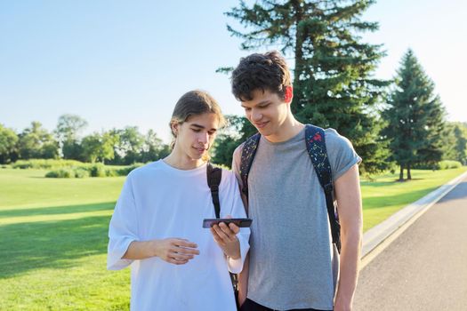 Teenagers friends talking looking at smartphone screen. Two guys 16, 17 years old with smartphone outdoors, on road on sunny summer day. Technology, lifestyle, friendship, youth, adolescence concept