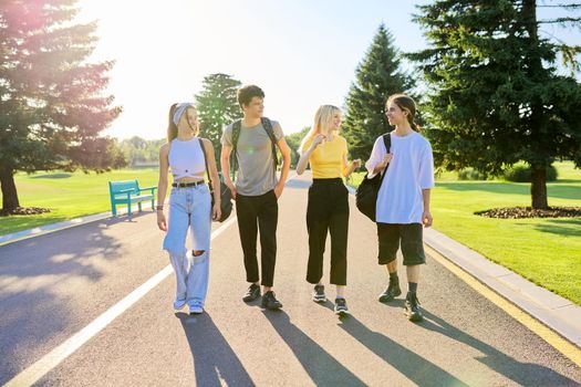 Outdoor, four teenagers walking together on road. Group of happy teenage friends on sunny summer day. Adolescence, youth, friendship, young people, high school college concept