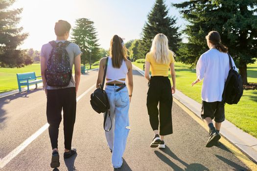 Outdoor, four teenagers walking together on road. Group of happy teenage friends on sunny summer day, back view. Adolescence, youth, friendship, young people, high school college concept