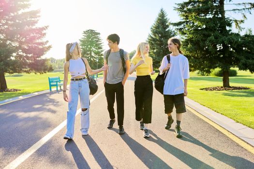 Outdoor, four teenagers walking together on road. Group of happy teenage friends on sunny summer day. Adolescence, youth, friendship, young people, high school college concept