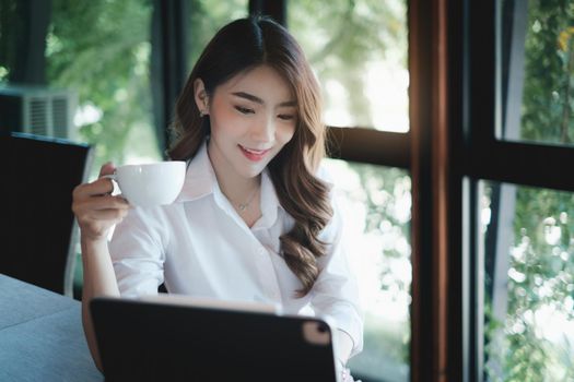 Image of beautiful business woman holds a cup of coffee and checks her email before going to work.
