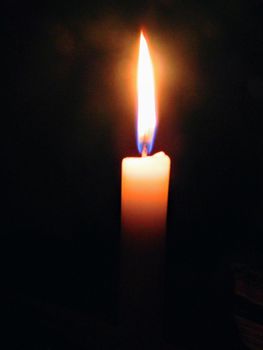 A candle brightly lit in a dark room yellow flame. High quality photo