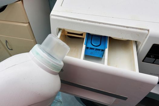 White plastic bottle with detergent against the background of the open compartment of the washing machine, close up.
