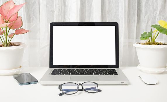 Modern workspace, mock up laptop computer blank white screen, eyeglasses and smartphone white table have potted plants on the desk, Notebook and mobile phone on desktop home office