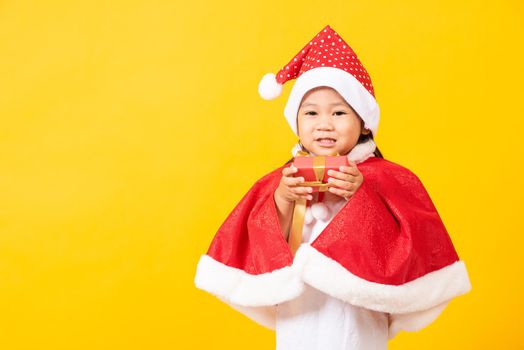 Asian little cute girl smile and excited, Kid dressed in red Santa Claus hat hold gift box on hands concept of holiday Christmas Xmas day or Happy new year, studio shot isolated on yellow background