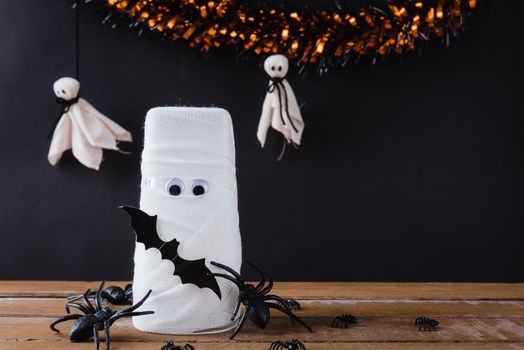 Funny Halloween day decor party concept, The mummy ghost on water glass wrapped around with bandage and have bats and spider stick it found only eyes, studio shot isolated on black background