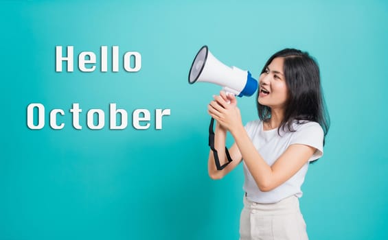 Hello October,  Portrait Asian beautiful young woman standing smile holding and shouting into megaphone looking to text, shoot the photo in a studio isolated on a blue background
