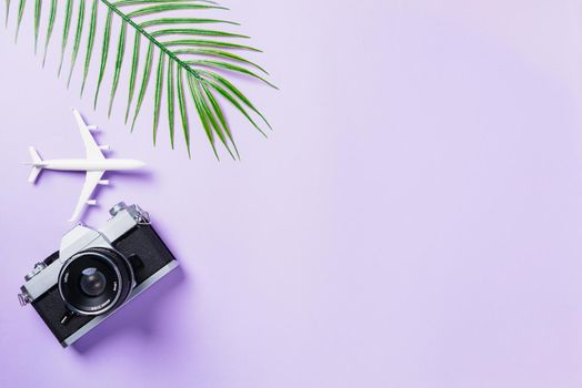 Top view flat lay mockup of retro camera films, airplane, leaves and traveler accessories isolated on a purple background with copy space, Business trip, and vacation summer travel concept