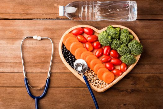 Top view of fresh organic fruits and vegetables in heart plate wood (carrot, Broccoli, tomato), doctor stethoscope and plastic water bottles on wooden table, Healthy lifestyle diet food concept